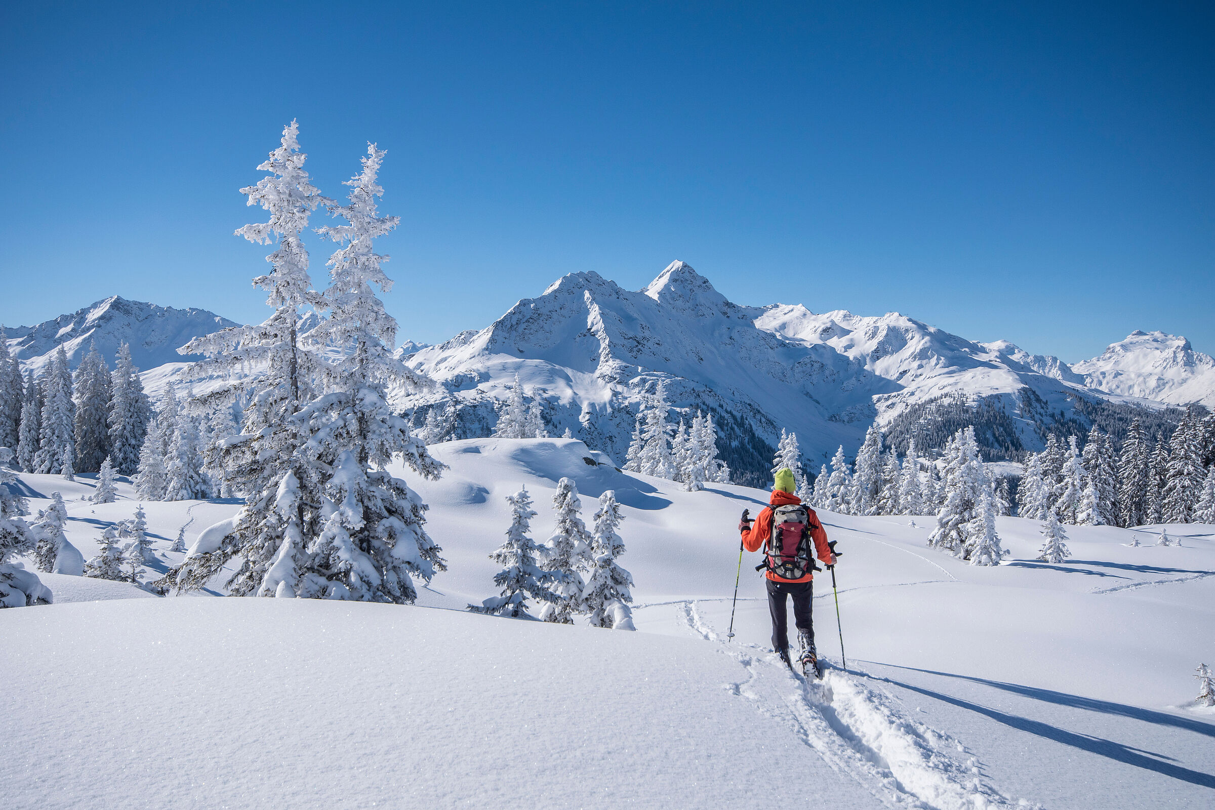 Beispiel für sanften Alpentourismus: Winterwanderer in verschneiter Landschaft vor sonnenbeschienenem Gipfel