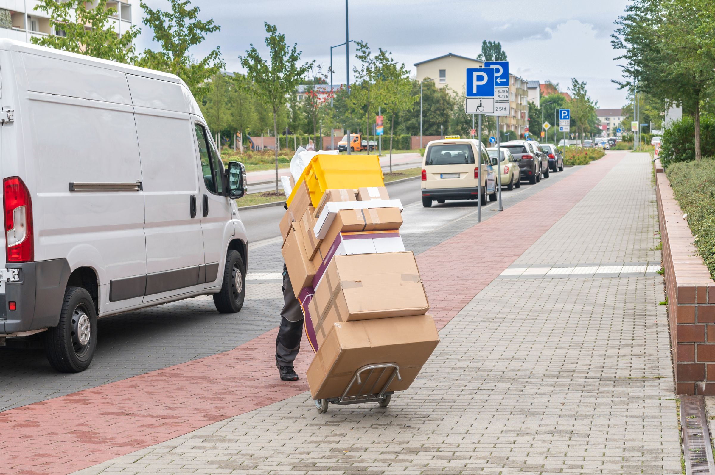 Zum Güterverkehr gehört auch der Lieferverkehr in den Kommunen: Ein Paketbote rollt Pakete über den Gehsteig. (Foto: Ronald Rampsch/stock.adobe.com)