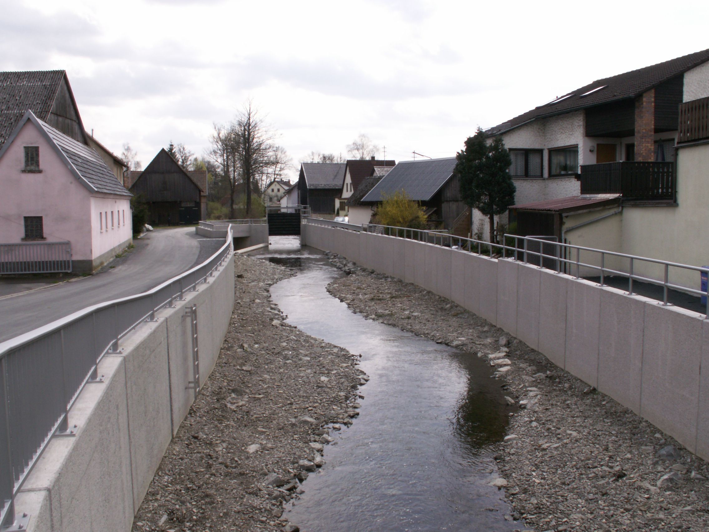 Ein Bach fließt in einem Kiesbett zwischen hohen Betonwänden, an den Seiten sind Häuser zu sehen – mit natürlichem Hochwasserschutz hat so eine Lösung nichts zu tun. (Foto: Tom Konopka)