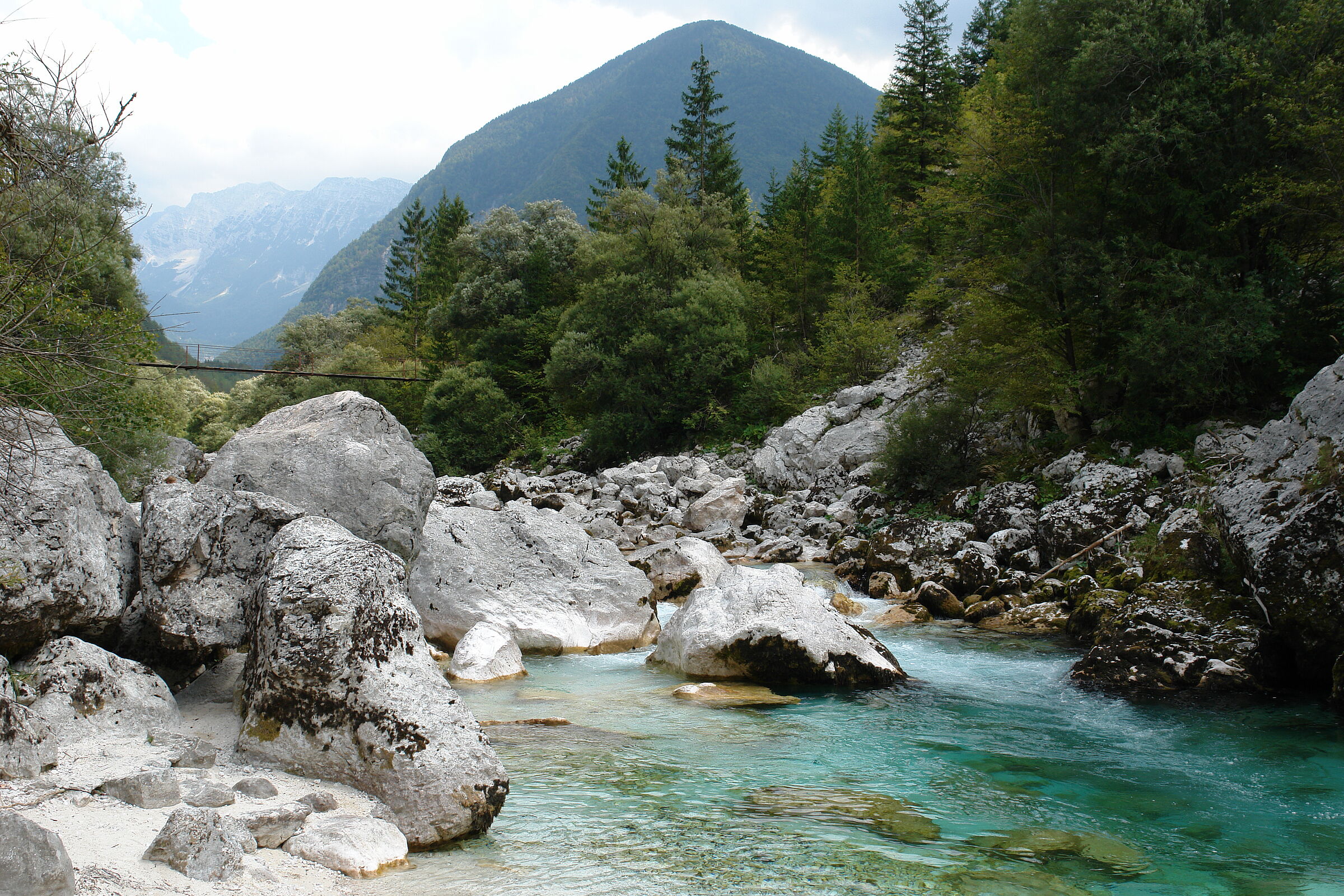 Am Grünen Band Europa: Ein türkisblauer Fluss fließt durch mächtige Gesteinsbrocken. An den Ufern wächst Wald und im Hintergrund sieht man verschneite Berge. Die Soca liegt am Grünen Band Europa. (Foto: Juergen Schmidl).