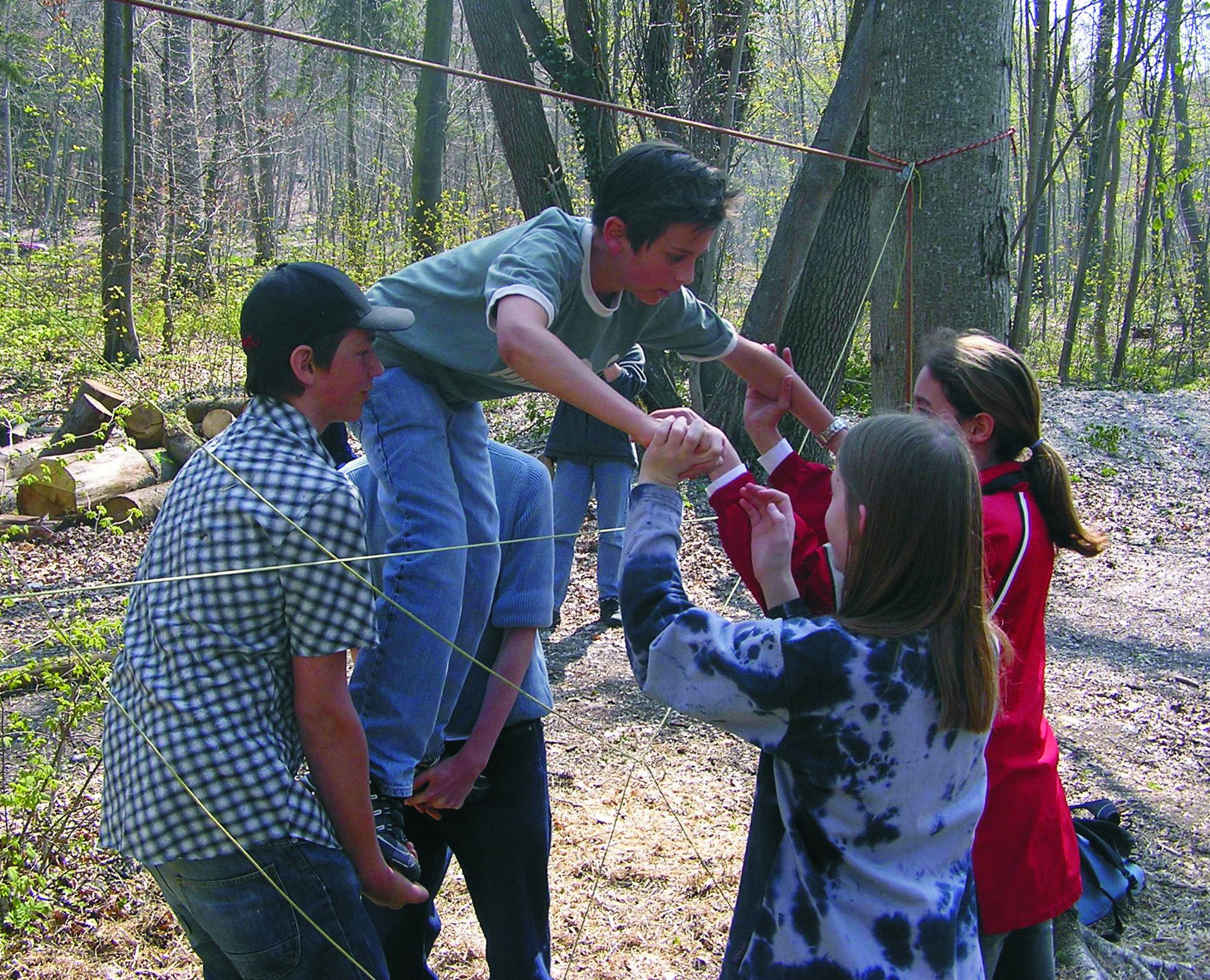 Eine Gruppe Kinder hilft sich gegenseitig ein aus Fäden gespanntes Spinnennetz im Wald zu überwinden. (Bild: BN-Archiv)