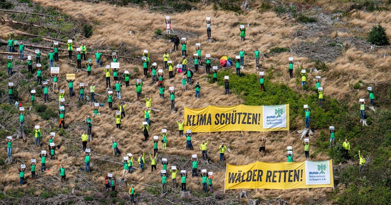 Auf einer Kahlflächen stehen viele Menschen in grünen und gelben Oberteilen. Sie halten Schilder hoch. Zwei große Transparente fordern auf: "Klima schützen" und "Wälder retten". Der BN protestiert im Frankenwald und fordert ein sofortiges Hilfspaket für die Wiederaufforstung. (Foto: Toni Mader) (Foto: Toni Mader)