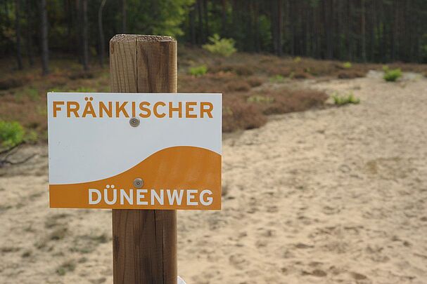 Ein Schild des Fränkischen Dünenwegs im Sand (Foto: Hofmann)