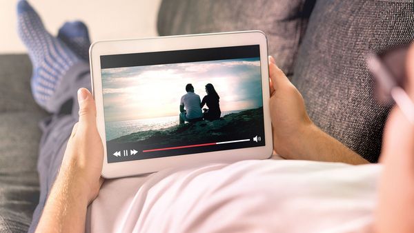 Strom sparen bei Internet, Computer und Smartphone: Ein Mann liegt auf einer Couch, hält ein Tablet in der Hand und streamt einen Film.