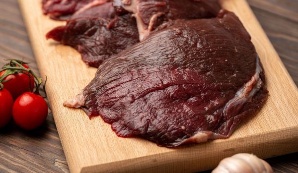 Wildfleisch kaufen: Mehrere Scheiben dunkelroten Rehfleischs liegen auf einem Holzbrett.