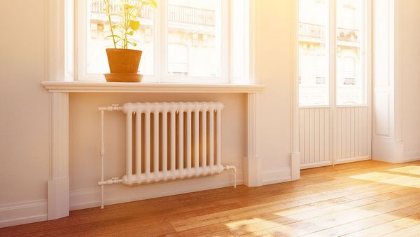 Richtig heizen: Heizkörper in einem hellen Zimmer mit Parkettboden, getaucht in warmes Tageslicht.