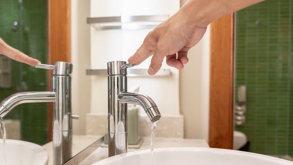 Wasser sparen: Eine Frau schließt mit ihrer Hand einen Wasserhahn.