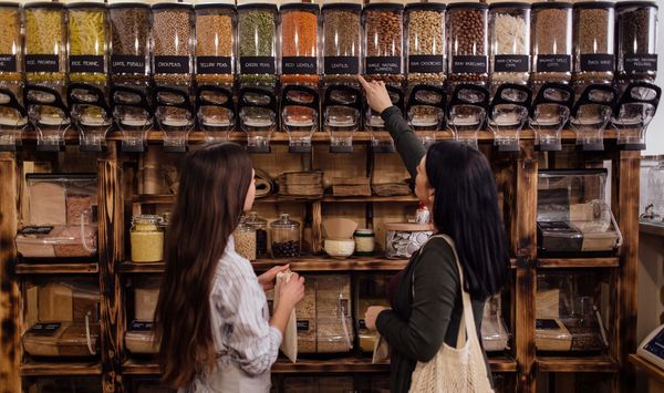 Umweltfreundliche Verpackungen: zwei Frauen stehen in einem Zero-Waste-Laden vor großen, durchsichtigen Behältern mit verschiedenen Lebensmitteln.