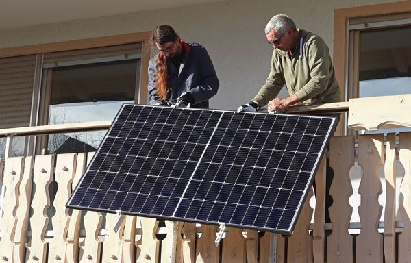 Balkonkraftwerk - Energiewende selbst gemacht: Zwei Männer befestigen eine Balkonsolaranlage am Geländer eines Balkons. (Foto: Astrid Gast/stock.adobe.com)