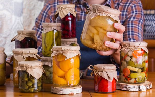 Lebensmittel konservieren: Ein Mann hält ein Glas mit konserviertem Gemüse in der Hand, weitere Gläser stehen auf einem Tisch.