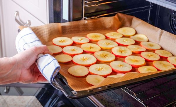 Lebensmittel konservieren: Apfelringe auf einem mit Papier abgedeckten Backblech, das gerade in den Ofen geschoben wird.