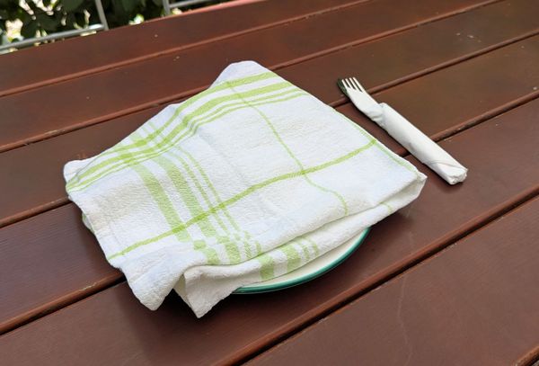 EIn Geschirrtuch deckt das Essen auf einem Teller im Freien ab.