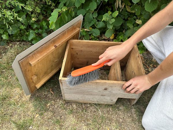 Eine Frau reinigt ein Igelhaus mit einer Bürste.