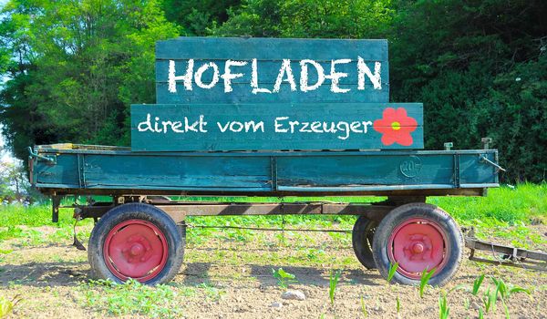 Auf dem Anhänger eines Traktors steht ein Schild mit der Aufschrift "Hofladen, direkt vom Erzeuger".