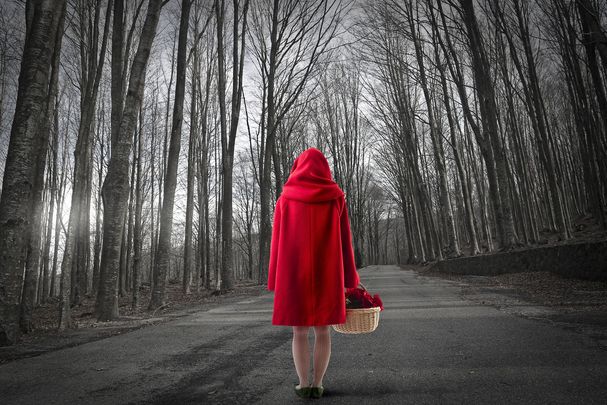 Eine Frau im roten Mantel steht im Wald mit Rücken zur Kamera. (Foto: olly/AdobeStock )