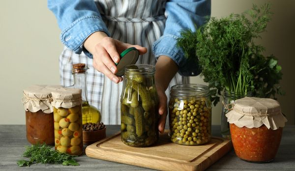 Lebensmittel konservieren: Eine Frau schließt ein Glas mit eingelegtenGurken, auf dem Tisch stehen weitere Gläser mit eingelegtem Gemüse.