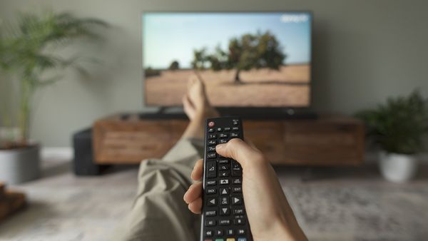 Strom sparen beim Fernsehen: Eine Frau sieht fern und hält die Fernbedienung in der Hand.