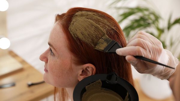 Henna richtig anwenden: Henna-Farbe wird mit einem Pinsel auf die roten Haare einer jungen Frau aufgetragen.