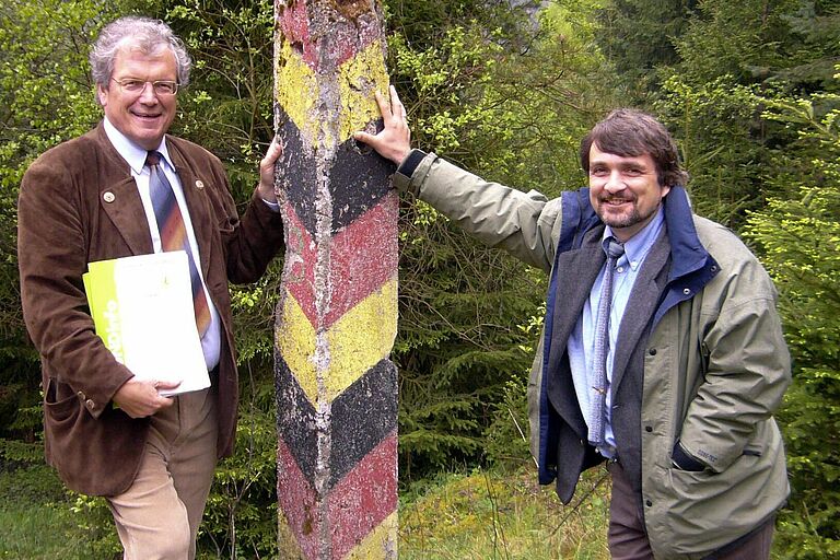 Am Grünen Band: Der ehemalige BN-Vorsitzende Hubert Weiger und BN-Artenschutzreferent und Erfinder des Grünen Bandes, Kai Frobel, lehnen an einem Grenzpfosten der ehemaligen innerdeutschen Grenze. Herr Weiger hält die Urkunde für den Deutschen Umweltpreis in der Hand. (Foto: BN e.V.)
