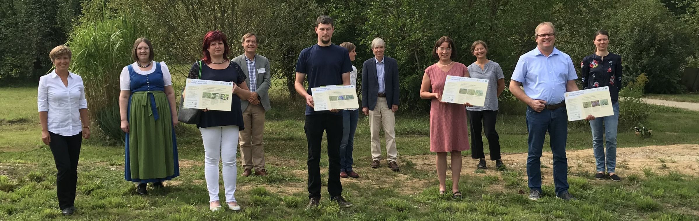 Eine Gruppe von Menschen steht mit Urkunden in der Hand auf einer Wiese. Die Preisträger des Ackerwildkraut-Wettbewerbs 2020. (Foto: Marion Ruppaner)