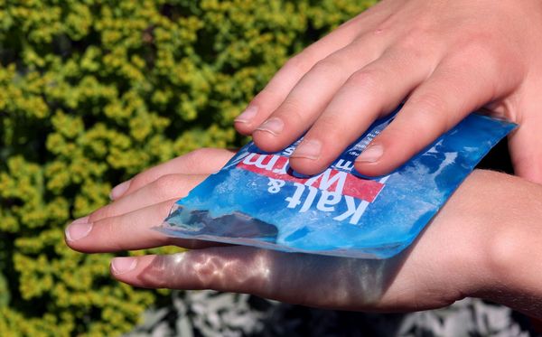 Jemand kühlt einen Wespenstich an seiner Hand mit einem Icepack