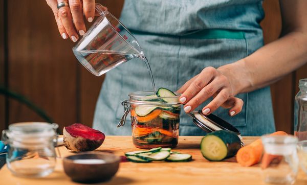 Lebensmittel konservieren: Eine Frau gießt Salzlake in ein Glas mit Gemüse.