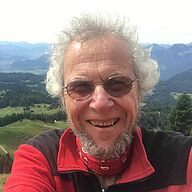 Ein Mann mit weißen Haaren, Bart und einem rot-schwarzen Pullover schaut in die Kamera. Foto: Christa Mayer-Röhrs