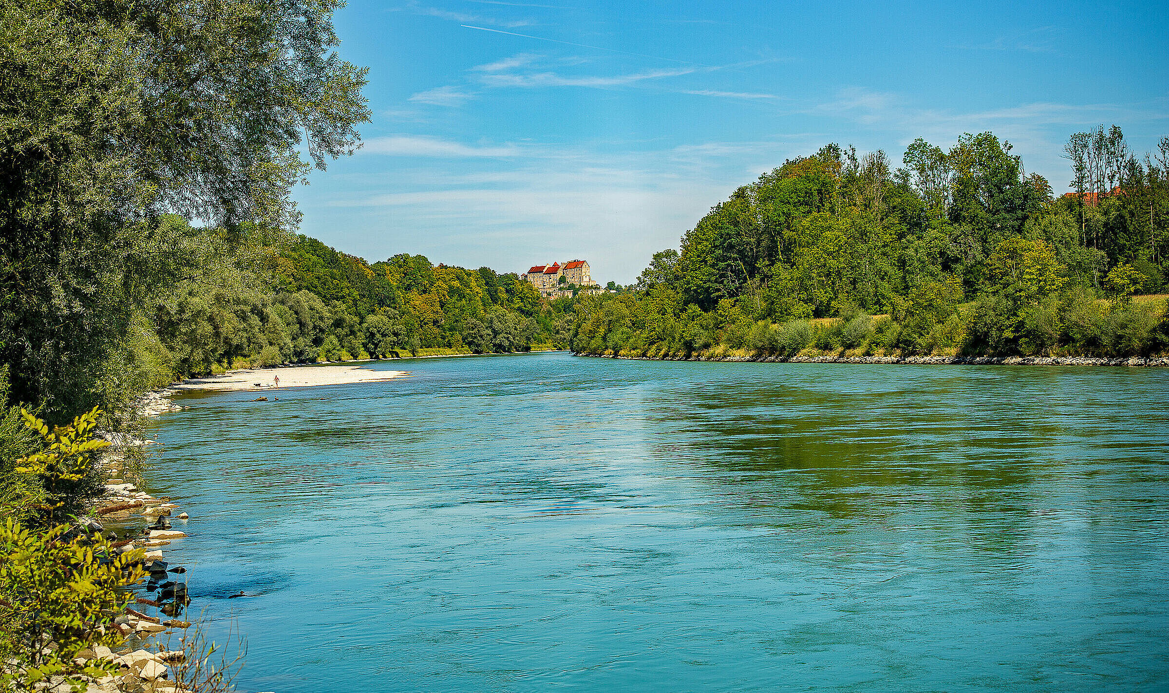 Ein breiter Fluss, fließt durch bewaldete Hügel, im Hintergrund eine Burg. (Foto: Jesus/stock.adobe.com)