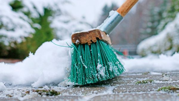 Umweltfreundliche Alternativen zu Streusalz: Ein Besen mit grünen Borsten fegt Schnee weg.