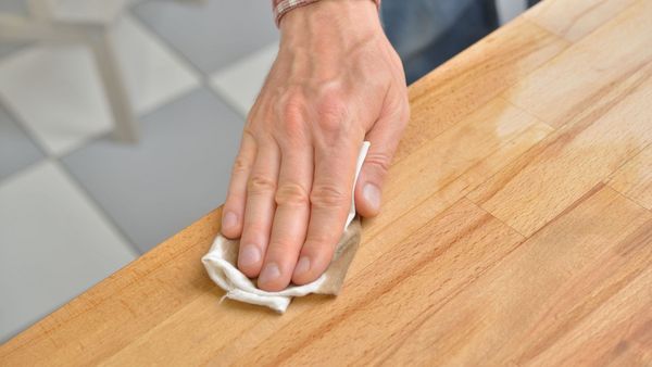 Wohnen mit Holz: Ein Mann ölt eine Tischplatte aus Holz ein.
