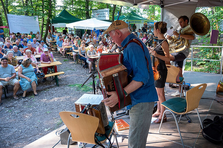 Eine Musikkapelle spielt auf einem Podium. Die Zuhörer*innen sitzen auf Bierbänken. Das Reichswaldfest hat eine jahrzehntelange Tradition. (Foto: BN)