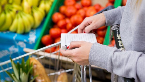 Lebensmittelverschwendung vermeiden: Eine Frau steht vor einem Gemüpseregal und hält eine Einkaufsliste in der Hand.